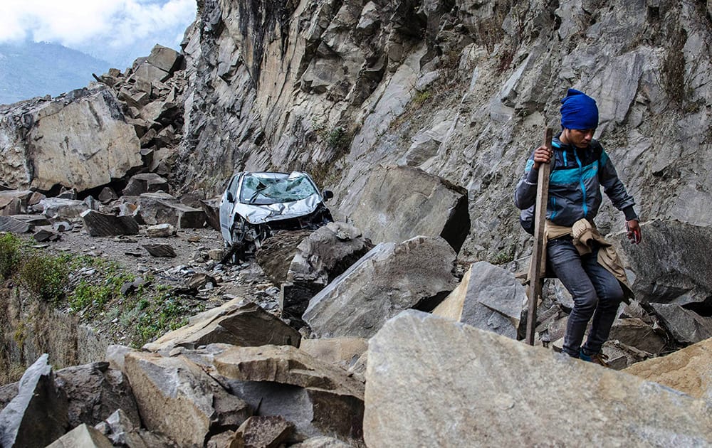 A Nepalese man walks over fallen rocks and past a crushed car on the way to Dhunche.