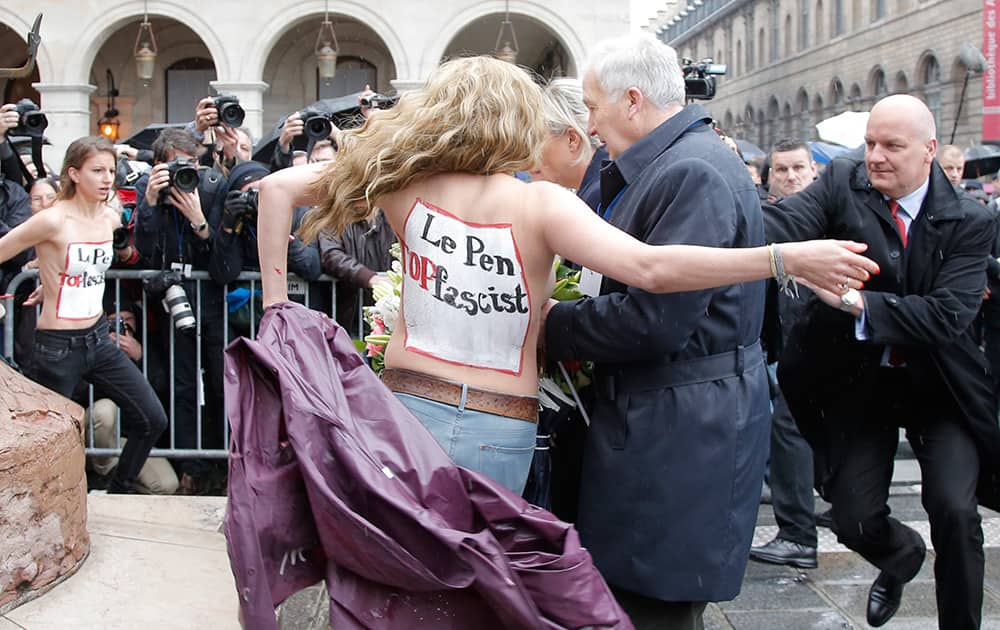 Femen activists with 'Le Pen Top Fascist painted on their bodies appear as France’s far-right National Front president Marine Le Pen places a wreath at Joan of Arc Statue during its annual May Day march, in Paris, France.