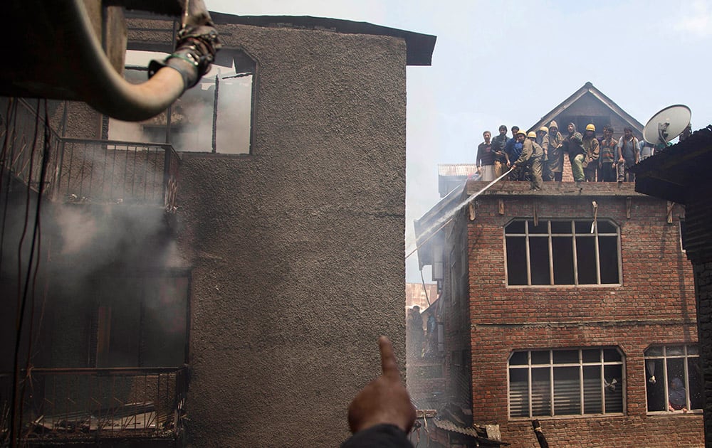 A Kashmiri Muslim points out a batch of flames to firefighters as they work to extinguish a fire in Srinagar. At least three houses were damaged in the fire Friday.