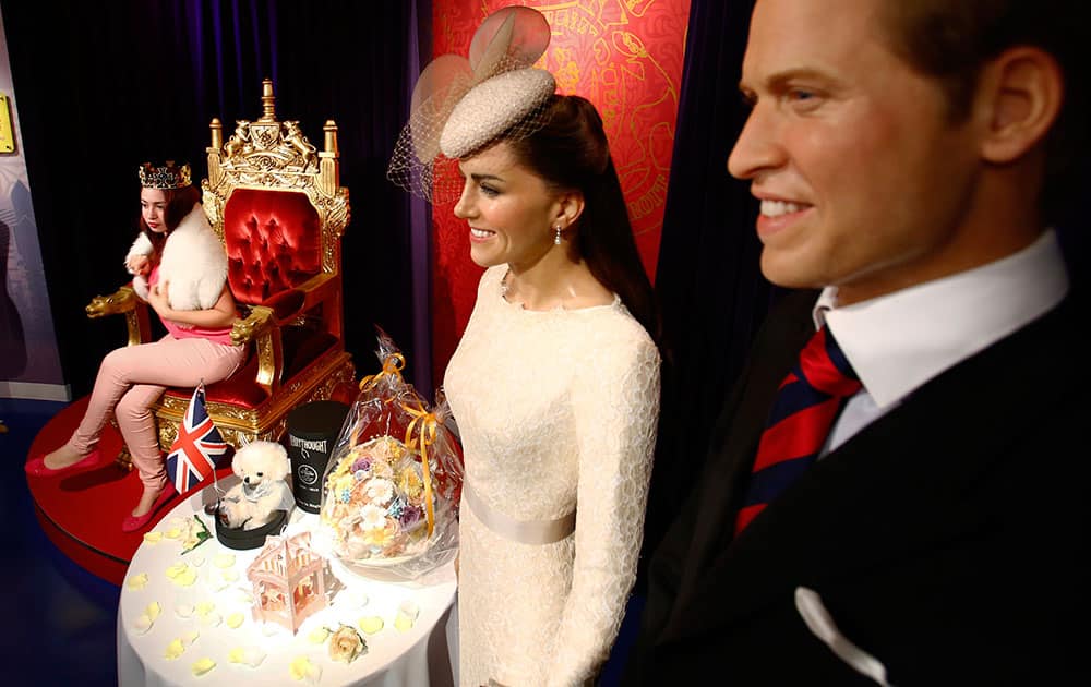 A visitor poses for a photo with wax figures of Britain's Prince William and his wife Kate as flowers are offered in celebration of the birth of the couple's second child, at Madame Tussauds in Tokyo