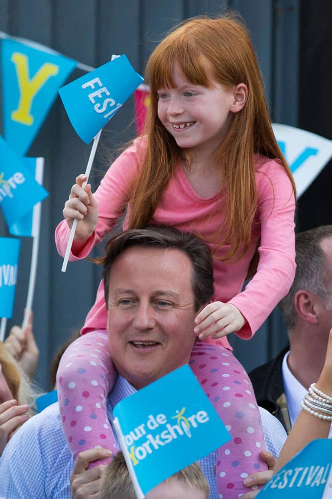 British Prime Minister David Cameron holds 7 year old Amelie Bone on his shoulders as he watches the Tour de Yorkshire cycle race pass through Addingham near Ilkley, during General Election campaigning in the lead up to the parliamentary elections on May 7, Addingham, England.