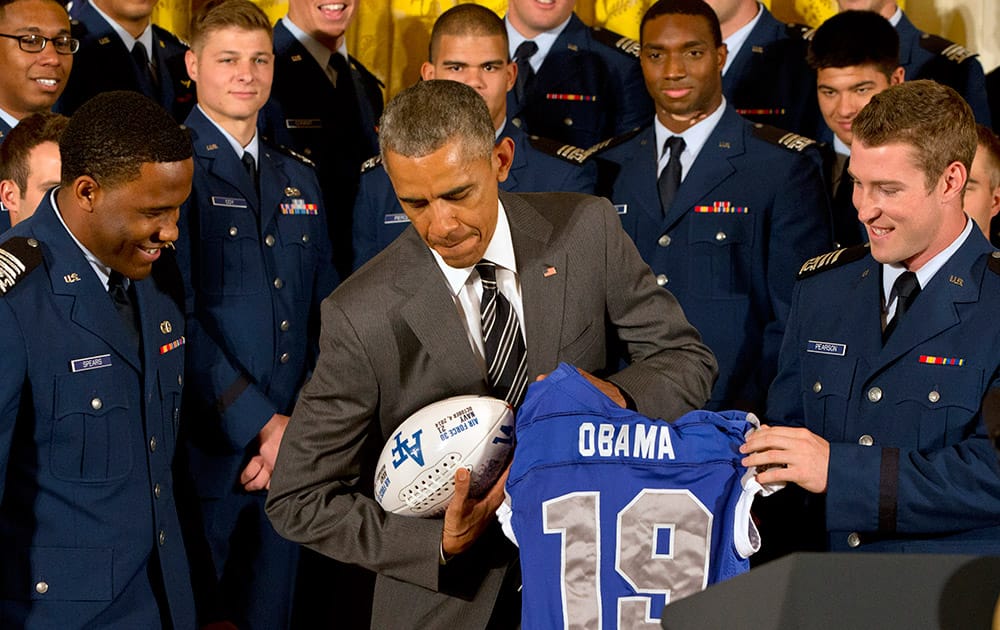 Air Force Defensive back Christian Spears, left, and quarterback Kale Pearson, right, smile as President Barack Obama poses with a football and jersey they gave him during an event in the East Room of the White House in Washington.