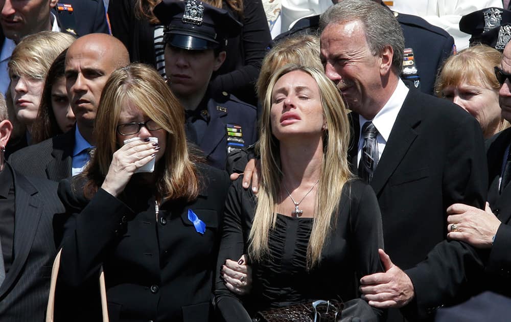 Police officer Brian Moore's mother Irene, left, sister Christine, center, and father Raymond react as his casket is placed in the hearse after his funeral mass, at the St. James Roman Catholic church in Seaford, N.Y. The 25-year-old died Monday, two days after he was shot in Queens.