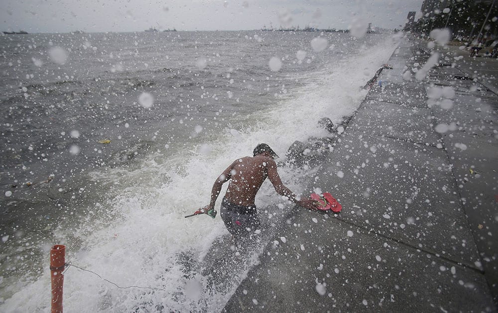 Strong waves hit a Filipino man as he retrieves rubber slippers along Manila bay, Philippines on Sunday, May 10, 2015. A powerful typhoon slammed into the northeastern tip of the Philippines.