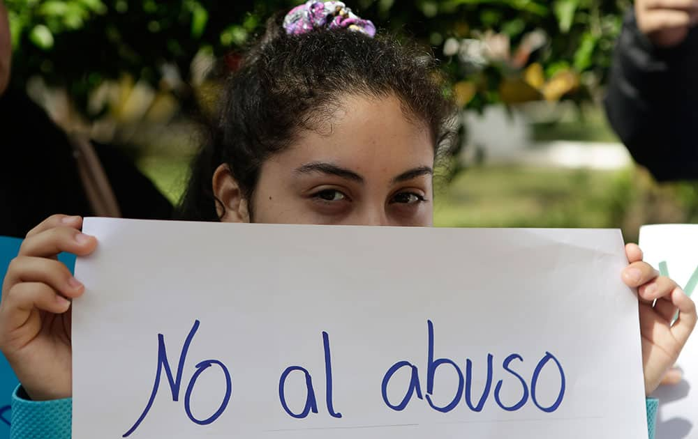 A girl holds a handwrittem message that reads in Spanish, 