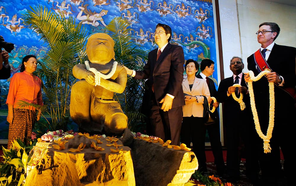 Cambodian Deputy Prime Minister Sok An, stands next to a 10th century Cambodian sandstone statue as the Director of the Cleveland Museum of Art William M. Griswold, holds a garland during a ceremony in Phnom Penh, Cambodia. The Cleveland Museum of Art on Tuesday handed over a 10th-century statue to Cambodia after it uncovered evidence the sculpture was probably looted during the country's civil war.