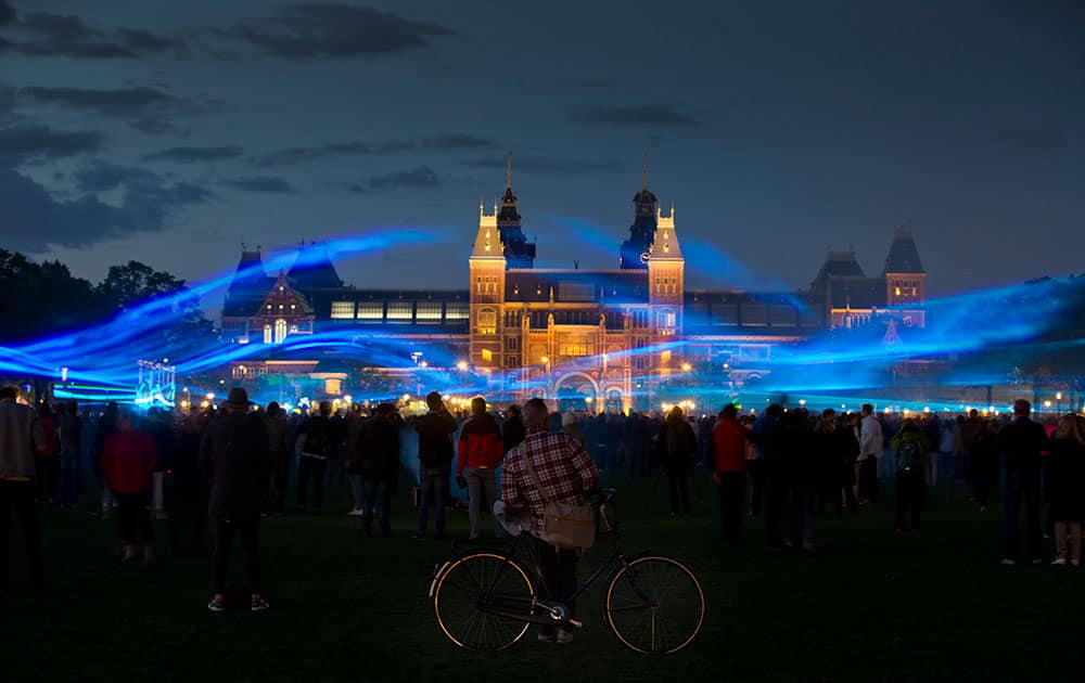 People watch a light show by Dutch artist Daan Roosegaarde called Waterlicht, or Water Light, at Rijksmuseum, rear, in Amsterdam, which creates the impression of water and floods on Museumplein square in Amsterdam, Netherlands.