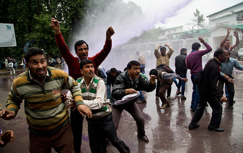 Protestors try to resist as police use colored water cannon to disperse government employees during a protest in Srinagar.