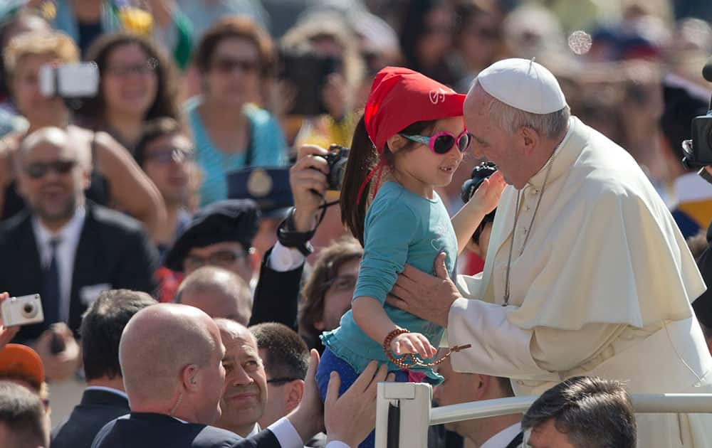 Pope Francis kisses a young girl as he arrives for his weekly general audience in St. Peter's Square at the Vatican.