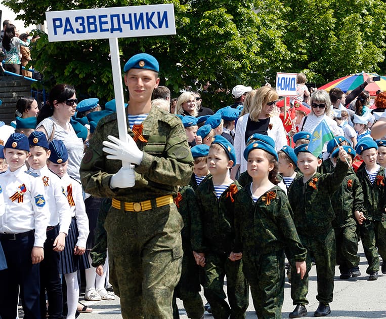 A man in a military uniform with a sign reading Scouts marches with children wearing specially made uniforms during the so-called Kid Parade in Rostov-on-Don, Russia