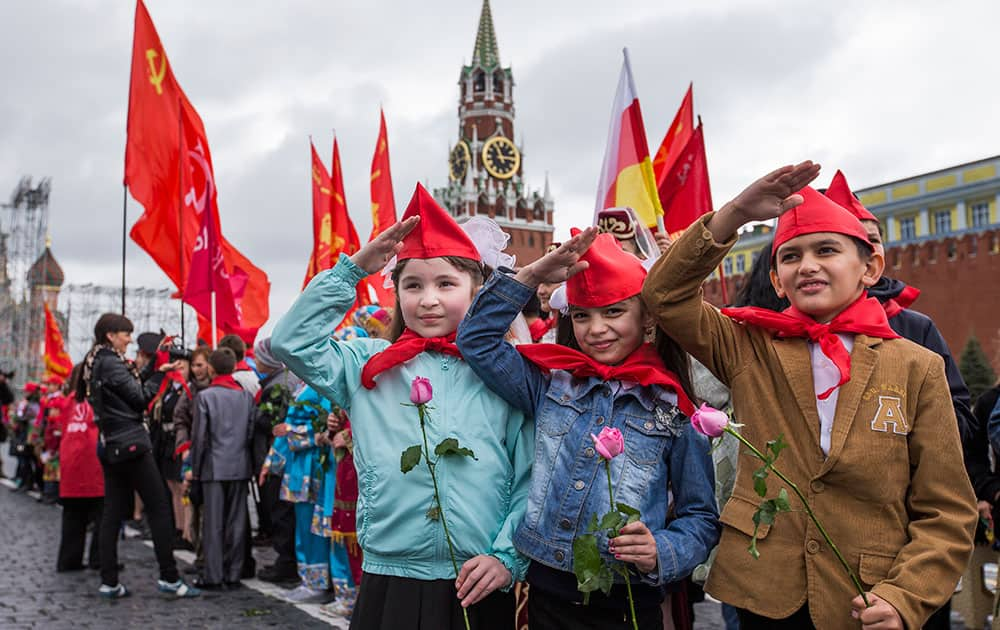 Girls and boys stand holding red neckerchiefs salute on Red Square, with the Historical Museum on the left, during a ceremony to celebrate joining the Pioneers organization, in Moscow, Russia.