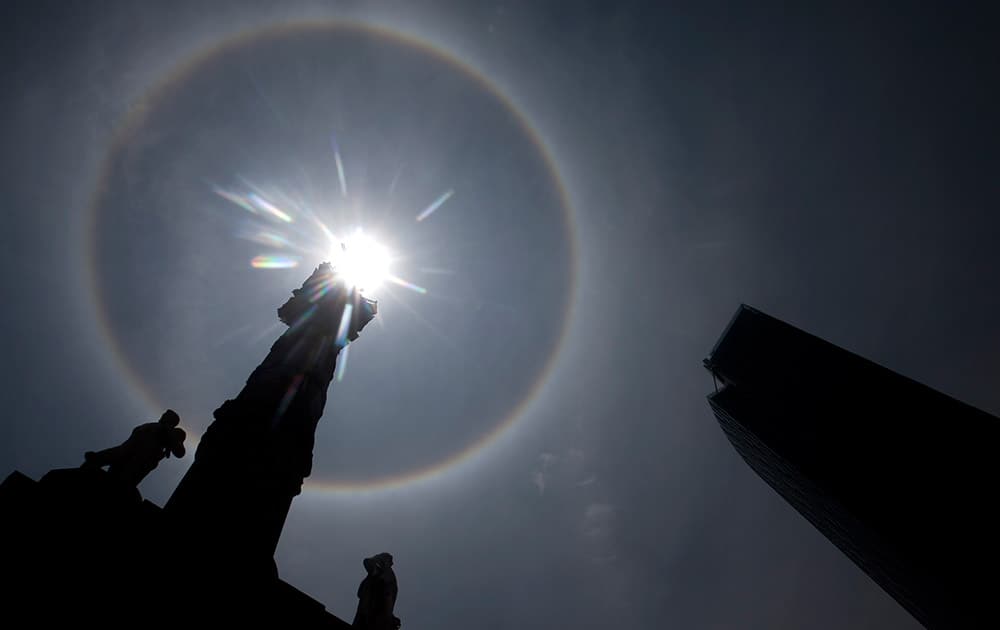 A circular sun halo forms in the sky over a silhouette of the Angel of Independence Monument in Mexico City.