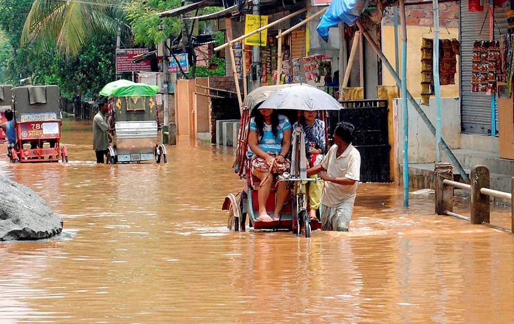 Commuters using rickshaws to cross the waterlogged road of Anil Nagar area following overnight rain in Guwahati.