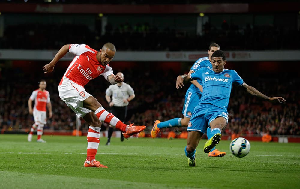 Arsenal's Theo Walcott, left, shoots past Patrick van Aanholt during the English Premier League soccer match between Arsenal and Sunderland at the Emirates Stadium in London