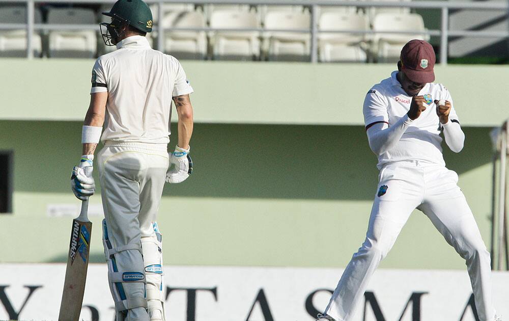 Australia's captain Michael Clarke, left, walks back to the pavilion after being caught behind by West Indies' captain Denesh Ramdin for 18 runs, as teammate Darren Bravo, right, celebrates during the opening day of their first cricket Test match in Roseau, Dominica.