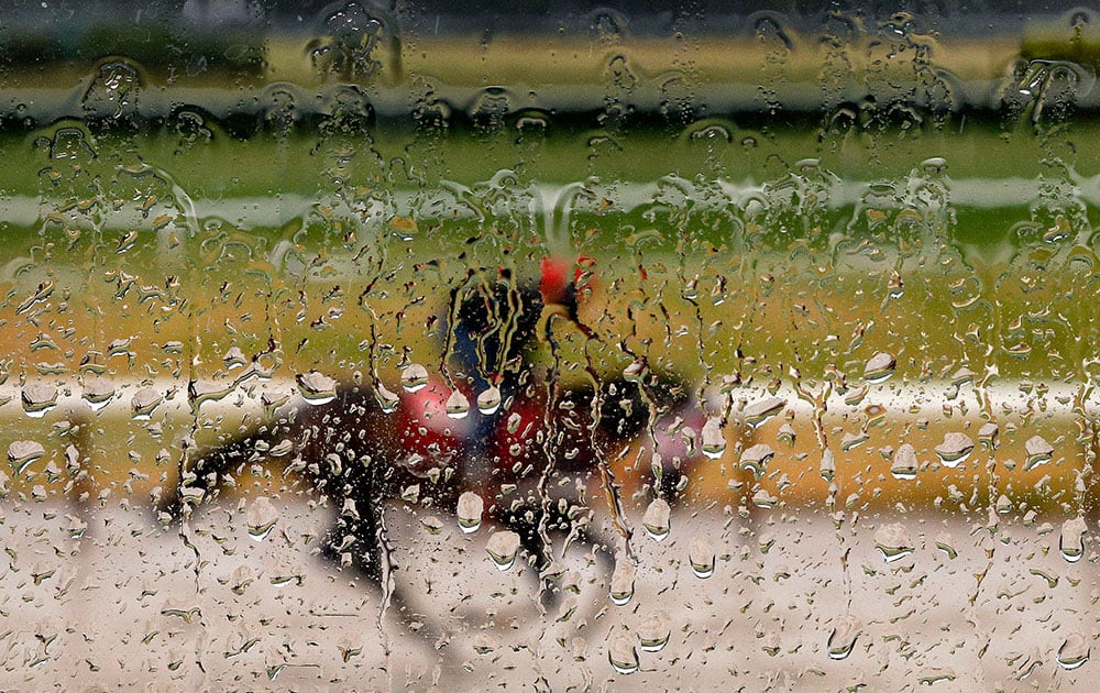 Rain water coats the window of an observation tower as an exercise rider guides a horse around the main track at Belmont Park, in Elmont, N.Y. 