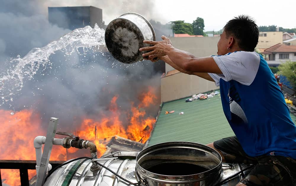 A resident throws a pail of water to burning houses below as fire engulfs a neighborhood of informal settlers in suburban Quezon city, northeast of Manila, Philippines.