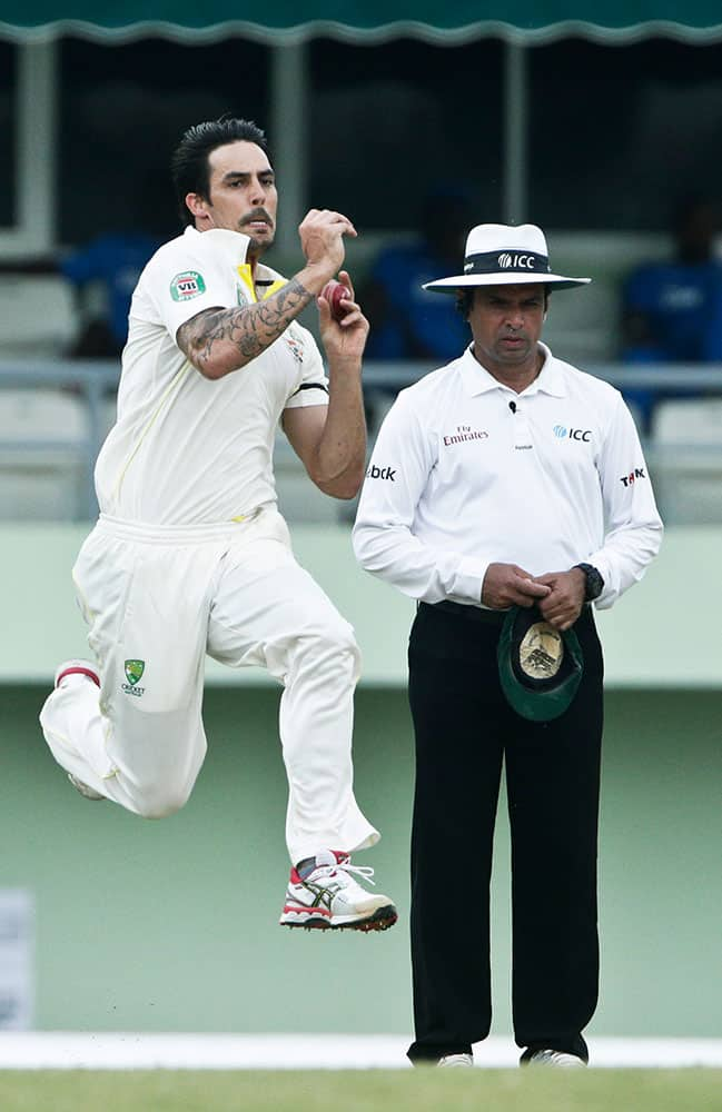 Australia's bowler Mitchell Johnson, left, bowls past umpire Aleem Darl, right, of Pakistan, during the second inning on the day two of their first cricket Test match against West Indies in Roseau, Dominica.