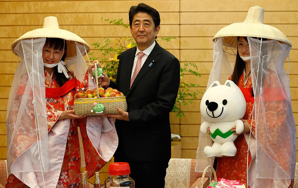 Japan's Prime Minister Shinzo Abe poses with Miss Plum Kozue Kimoto and Fuyuka Baba who are representing the Kishu Plum Organization as he is presented a basket of plums during their courtesy call at Abe's official residence in Tokyo.