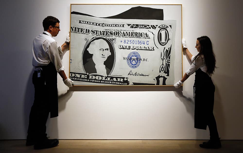 Two employees stands with an artwork by Andy Warhol called 'Silver Certificate' estimated at £13-£18 million (19.8-27.4 million US dollars) at Sotheby's auction house in London.