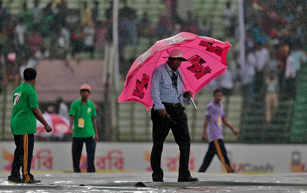 Curator of the cricket field walks with an umbrella over ground covers as it rains during the first day of the test cricket match between Bangladesh and India in Fatullah, Bangladesh.