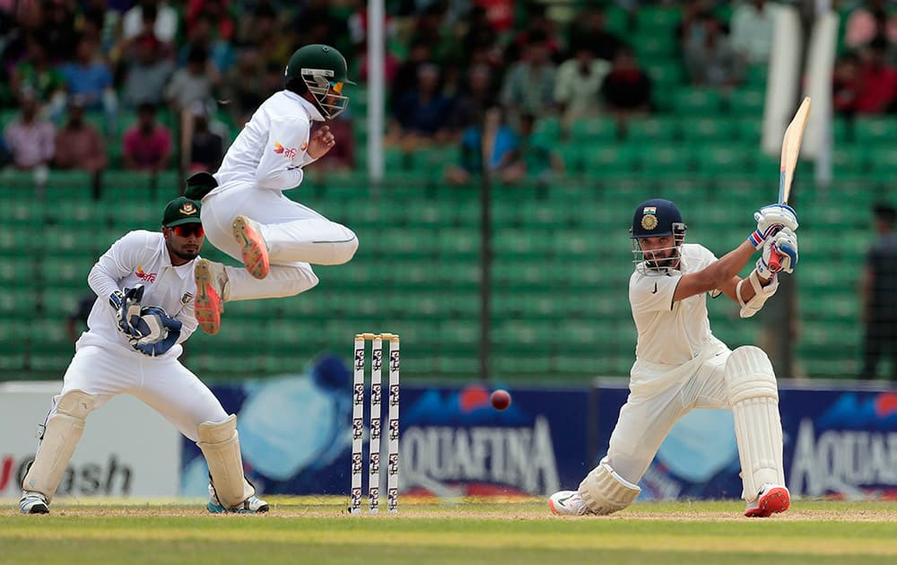 Ajinkya Rahane plays a shot as Bangladesh's Mominul Haque jumps during the third day test cricket match against Bangladesh in Fatullah, Bangladesh.