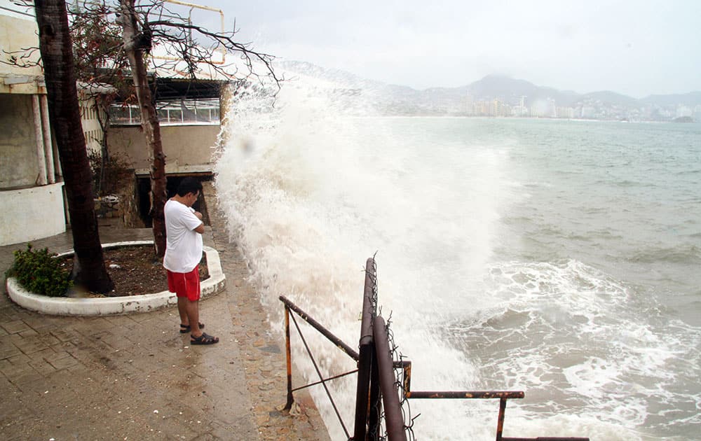 A man watches as waves crash against a sea wall in the Pacific resort city of Acapulco, Mexico.
