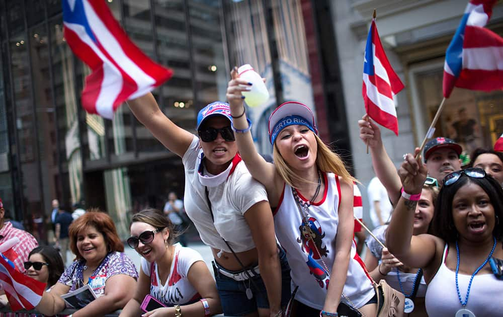 Arsenia Fuentes, center left, and Sarah Dones, center right, cheer for a passing float as the annual National Puerto Rican Day Parade makes its way up New York's Fifth Ave.