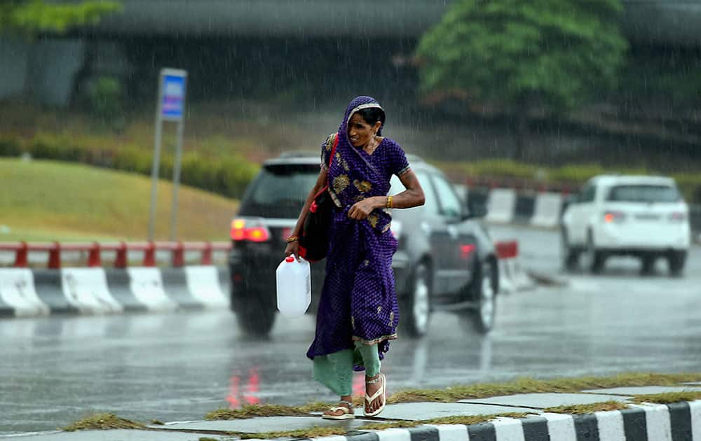 A woman walks cautiously at a road divider as it rains at India Gate in New Delhi.