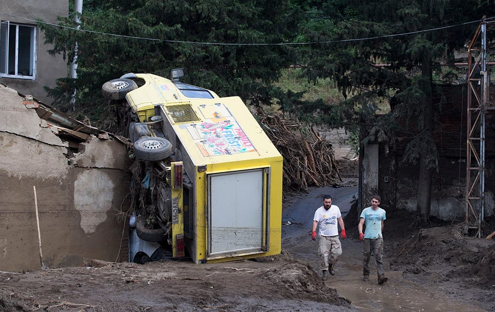 Volunteers walk past an overturned truck, after Sundays flooding, in Tbilisi, Georgia. Workers and volunteers labored Monday in a flood-ravaged area of the Georgian capital to help victims while nervously watching for traces of dangerous animals that may have escaped the city zoo when it was inundated by the surging waters. Officials in the ex-Soviet republic said 14 people were confirmed dead.