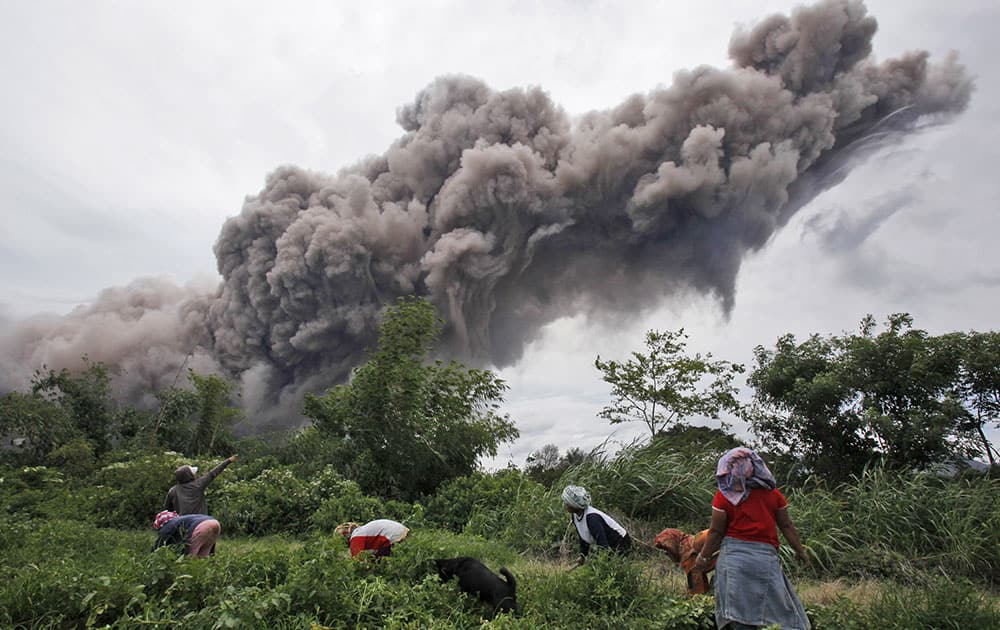 Farmers work on their field as Mount Sinabung spews volcanic material into the air in Sukandebi, North Sumatra, Indonesia.