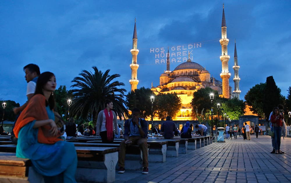 People gather backdroped by the the iconic Sultan Ahmed Mosque, better known as the Blue Mosque, decorated with lights marking the month of Ramadan, in the historic Sultanahmet district of Istanbul, Turkey.