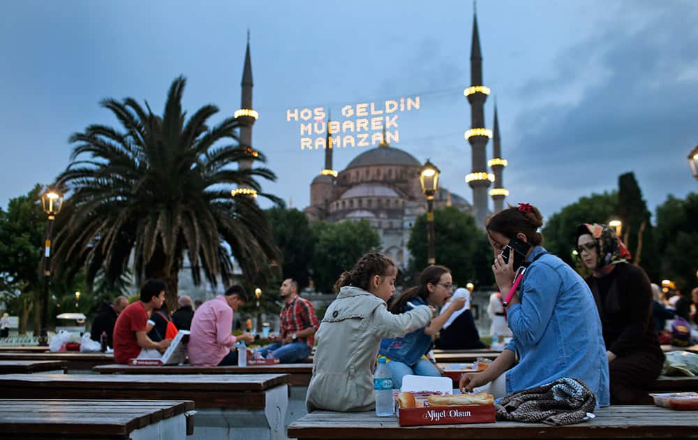 People break their fast backdroped by the the iconic Sultan Ahmed Mosque, better known as the Blue Mosque, decorated with lights marking the month of Ramadan, in the historic Sultanahmet district of Istanbul, Turkey.