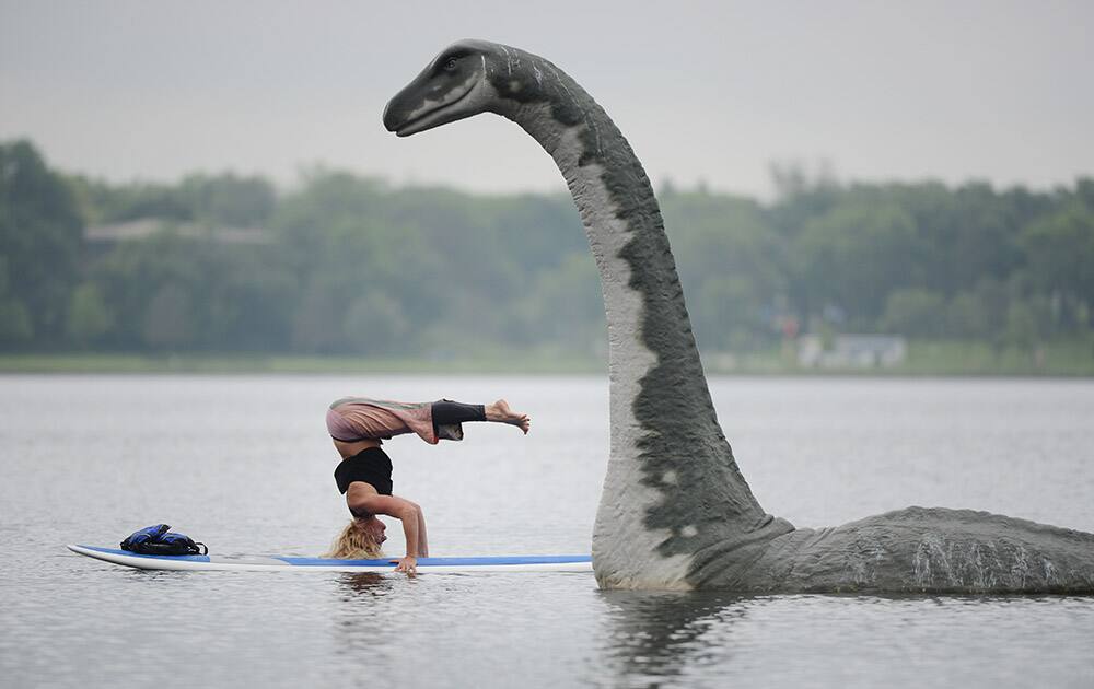 Stachia Fey, of the Wai Nani Surf and Paddle Tribe, strikes a yoga pose on her paddle board next to Minne, a 13' fiberglass lake creature on Lake Calhoun in Minneapolis, Minn.