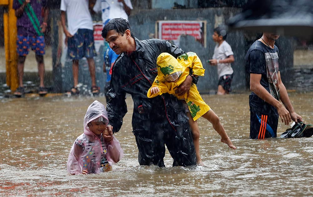 A man carries children and crosses a waterlogged street as it rains in Mumbai.