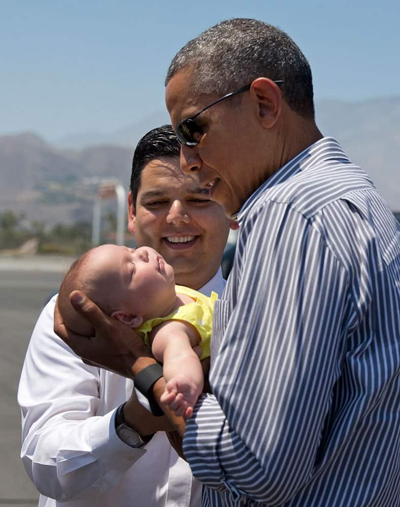 President Barack Obama holds one of the twin daughters of Rep. Raul Ruiz, D-Calif., background, as he arrives on Air Force One at Palm Springs International airport in Palm Springs, Calif.