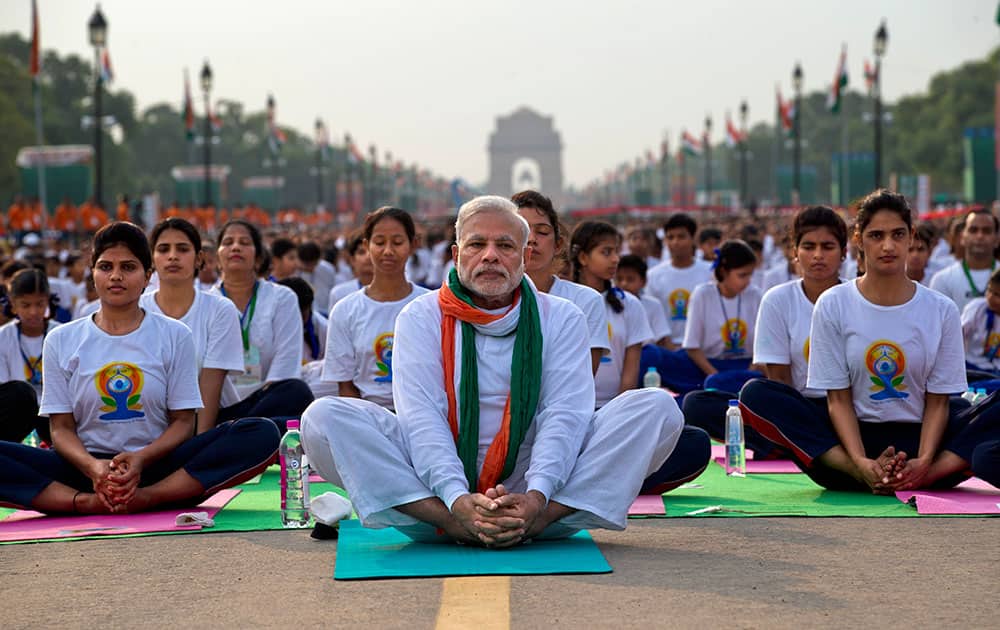 Prime Minister Narendra Modi, center, sits on a mat as he performs yoga along with thousands of Indians on Rajpath, in New Delhi, India.