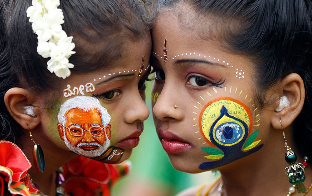 An Indian girl, left, displays a picture of Indian Prime Minister Narendra Modi painted on her face as another sports the logo of International Yoga Day in Bangalore, India.