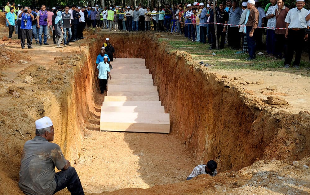 Malaysian religious officers and villagers place coffins containing remains of Rohingya migrants for a mass burial ceremony in Kedah, Malaysia .