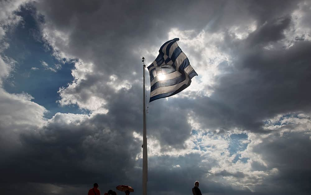 Tourists stand beneath a Greek flag fluttering against the sun at the ancient Acropolis hill , in Athens.