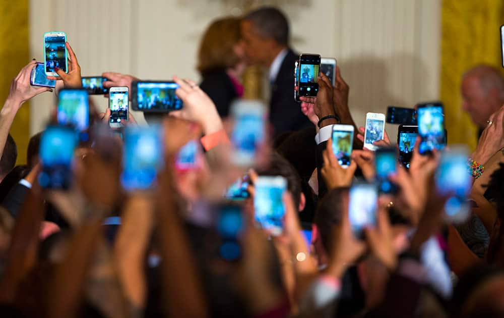 Guests hold up cell phones as President Barack Obama, right, is greeted by White House chief technology officer Megan Smith as he arrives for a reception to celebrate LGBT Pride Month in the East Room of the White House.