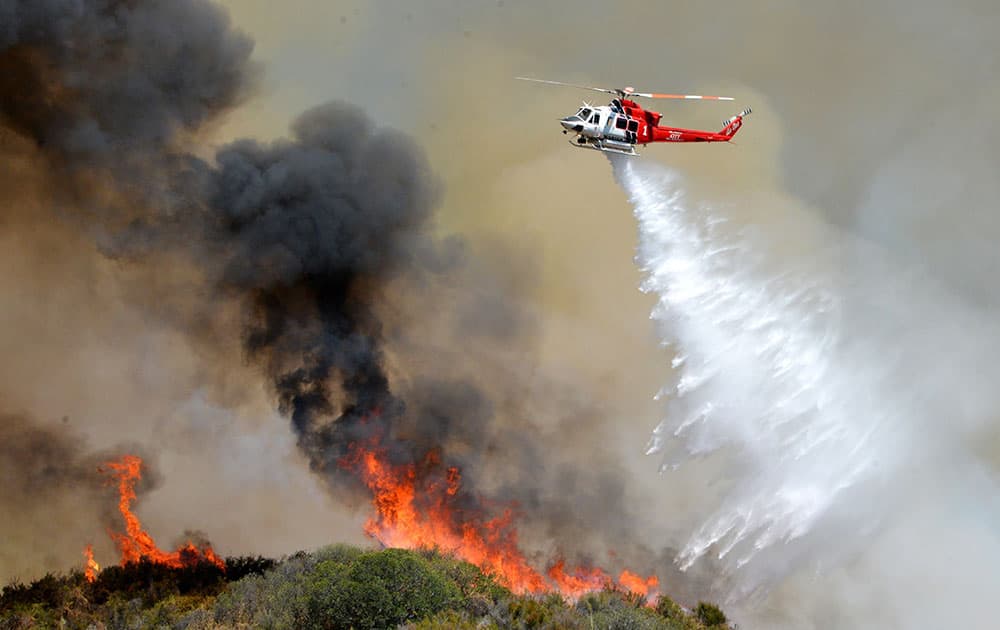 A Los Angeles City Fire helicopter drops water on flames, in Santa Clarita, Calif. About 1,000 people have been evacuated from homes as a 100-acre wildfire burns through brushy canyonlands north of Los Angeles. 