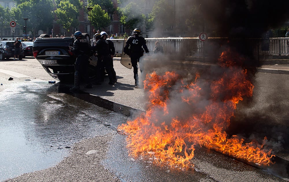 Riot police officers stand by an overthrown car during a taxi drivers demonstration, in Paris.