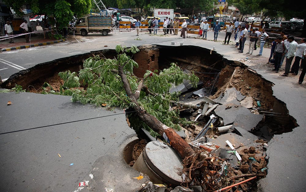 People look at a large portion of a road that caved in following heavy rains in Ahmadabad, Gujarat.