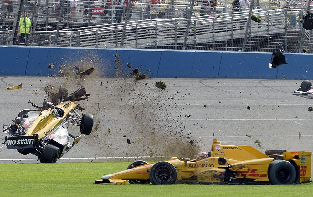 Ryan Briscoe, left, flips through the infield grass near Ryan Hunter-Reay, during the IndyCar auto race at Auto Club Speedway in Fontana, Calif.