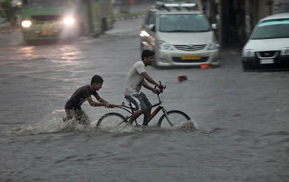 An Indian man pedals a cycle as a boy pushes it through a flooded street during a monsoon shower in Jammu, India.