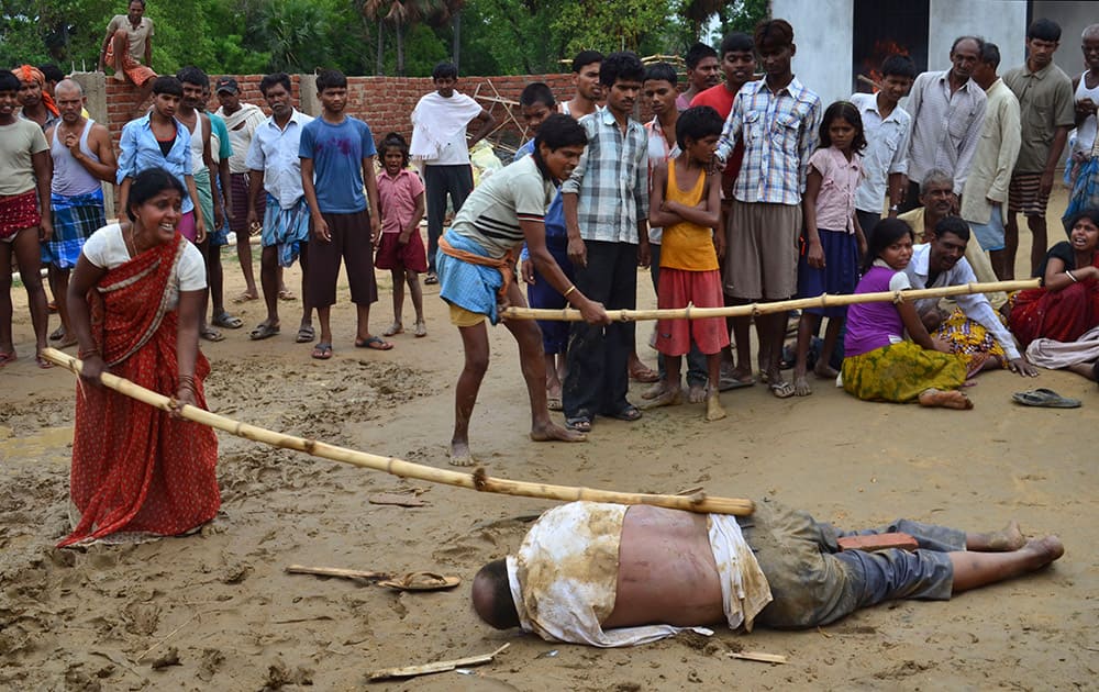 A man and a woman strike the body of a school director with sticks as it lies on the ground in Nirpur village, about 90 kilometers (55 miles) southeast of Patna, the capital of Bihar state, India.