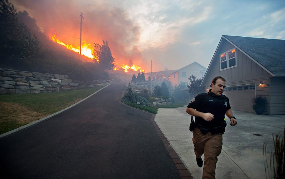 a Chelan County Sheriffs deputy races to check that all residents have left their home as flames approach houses at Quail Hollow Lane in Wenatchee, Wash. 