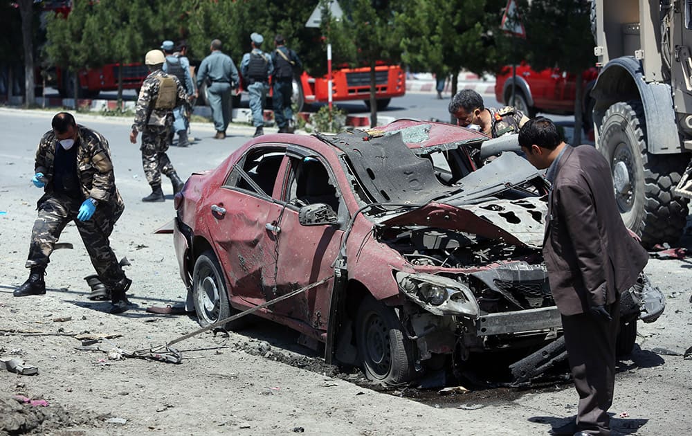 Afghanistan security personnel inspect a destroyed vehicle at the site of a suicide attack on a NATO convoy in Kabul, Afghanistan.