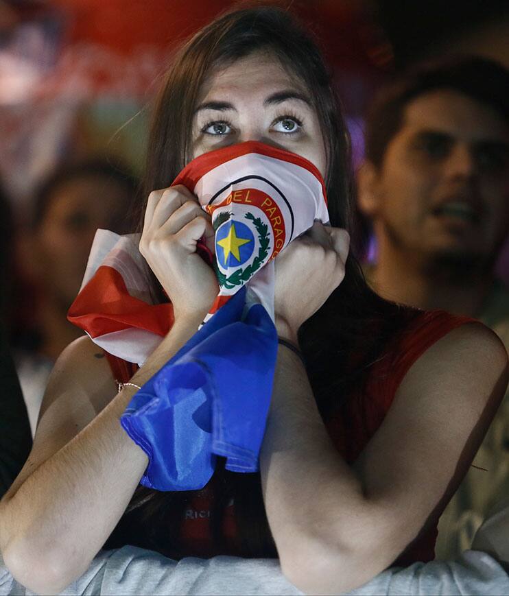 A fan of Paraguay's national soccer team covers her mouth with a Paraguayan flag while watching the Copa America semifinal soccer match between Paraguay and Argentina, on a television screen in Asuncion, Paraguay.